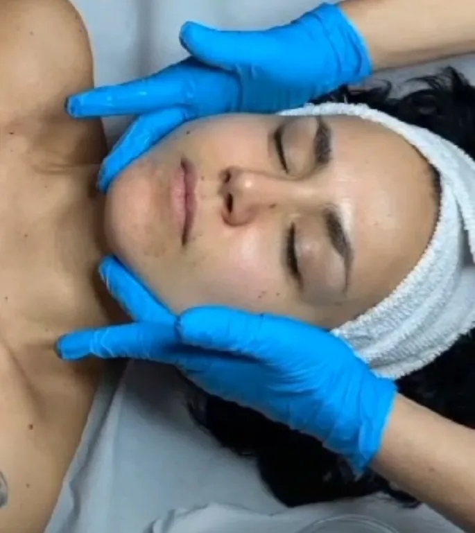 Massaggio buccale: le mani dell'operatrice, con i guanti, sul viso di una cliente distesa